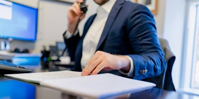 a man sitting at a desk writing on a piece of paper FEATURED IMAGE