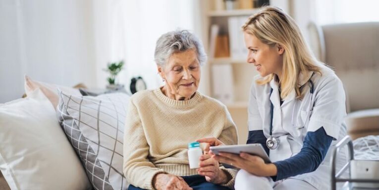 a young health visitor with tablet explaining a senior woman how to take medicine and pills FEATURED IMAGE
