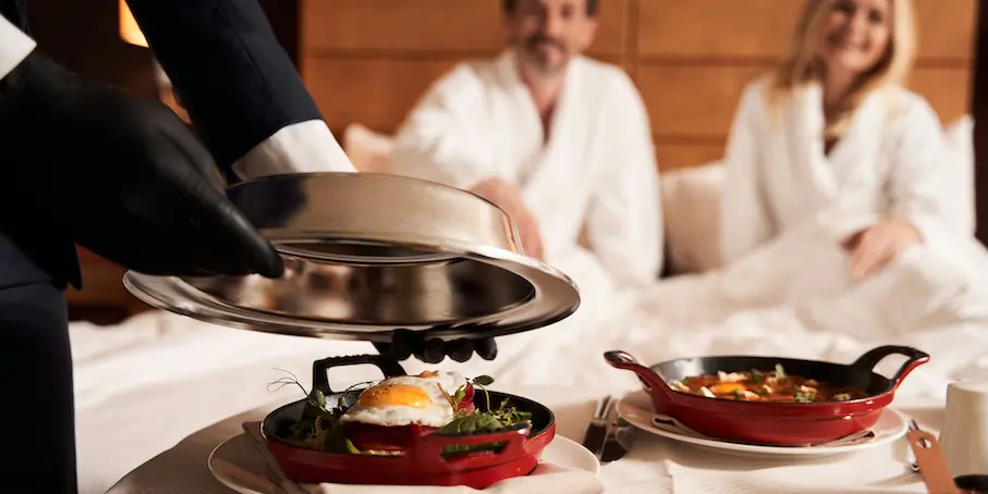 hands of a hotel waiter taking a metal cover off the frying pan with delicious fried egg FEATURED IMAGE