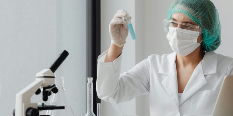 a woman in a white lab coat and green hair wearing a mask FEATURED IMAGE