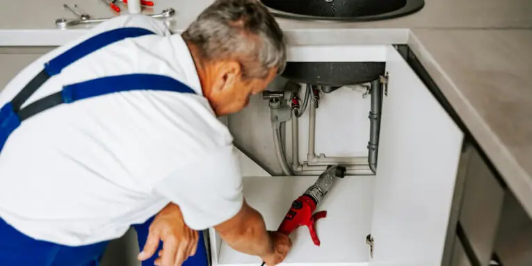 a plumber is working under a kitchen sink FEATURED IMAGE