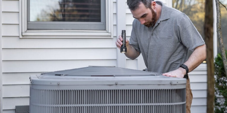 A technician inspects an outdoor HVAC unit for maintenance FEATURED IMAGE