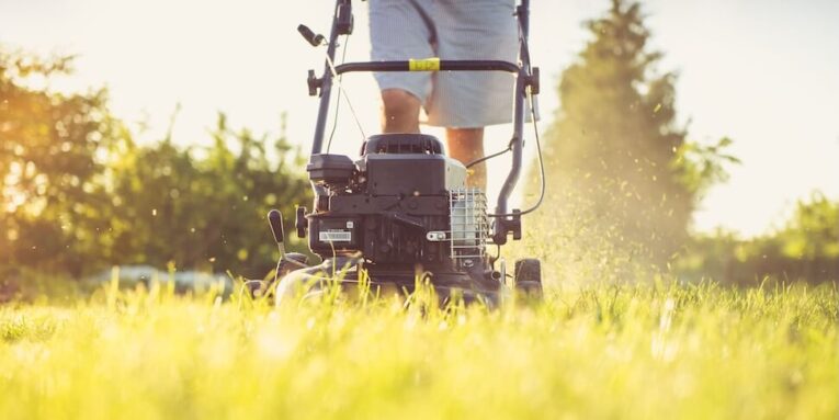 Close-up of a person mowing the lawn with a gas lawn mower on a sunny summer day FEATURED IMAGE