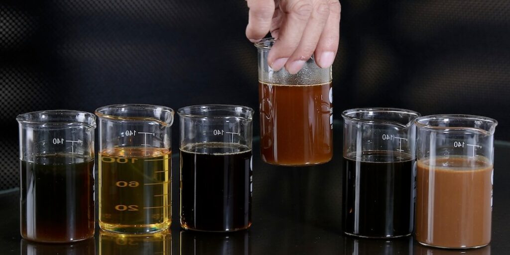 hand holding beaker above five other liquid filled beakers FEATURED IMAGE